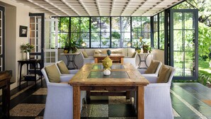 A spacious room with a large wooden table surrounded by white wicker chairs, a glass-top coffee table, and potted plants. - Owner's Cottage at Grande Provence (Franschhoek)