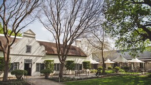 A traditional building with a brick facade, a central entrance, and a paved courtyard with seating areas and umbrellas. - Owner's Cottage at Grande Provence (Franschhoek)