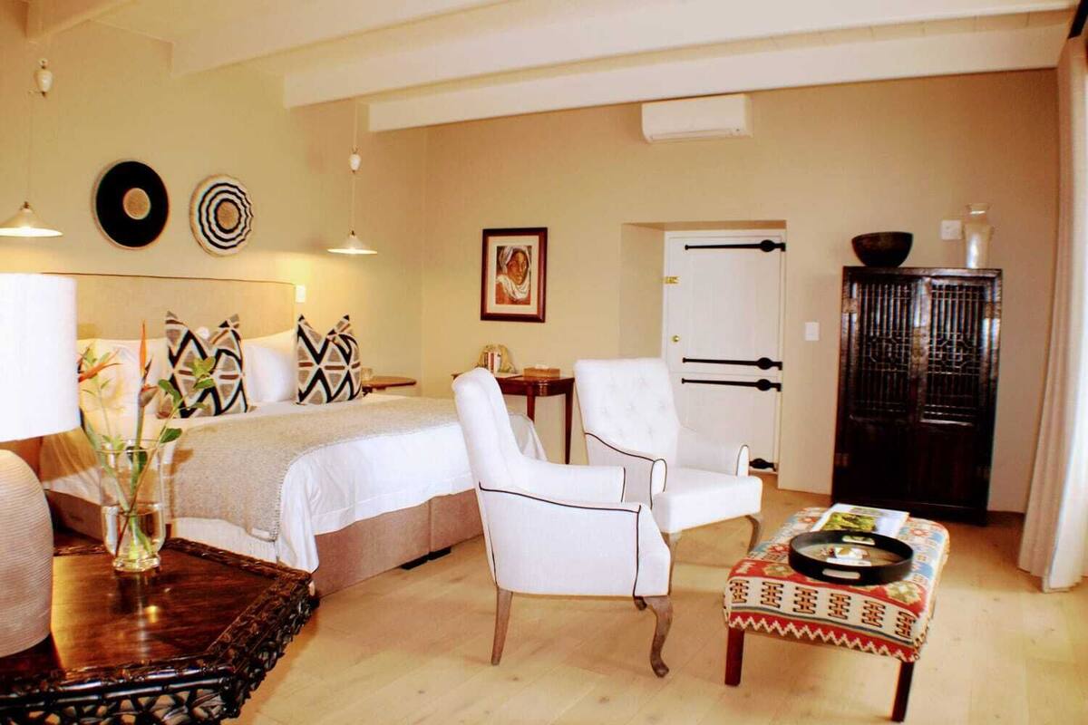 A hotel room with a bed, a white armchair, a small table with a tray, a cabinet, and a door with a black handle.
