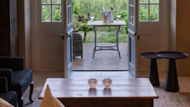 A room with a large arched window leading to an outdoor area with a table and chairs. - Owner's Cottage at Grande Provence (Franschhoek)