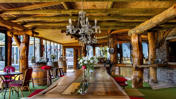 A rustic wooden interior with a large wooden table, chairs, and a chandelier. - T'Niqua Stable Inn (Plettenberg Bay)