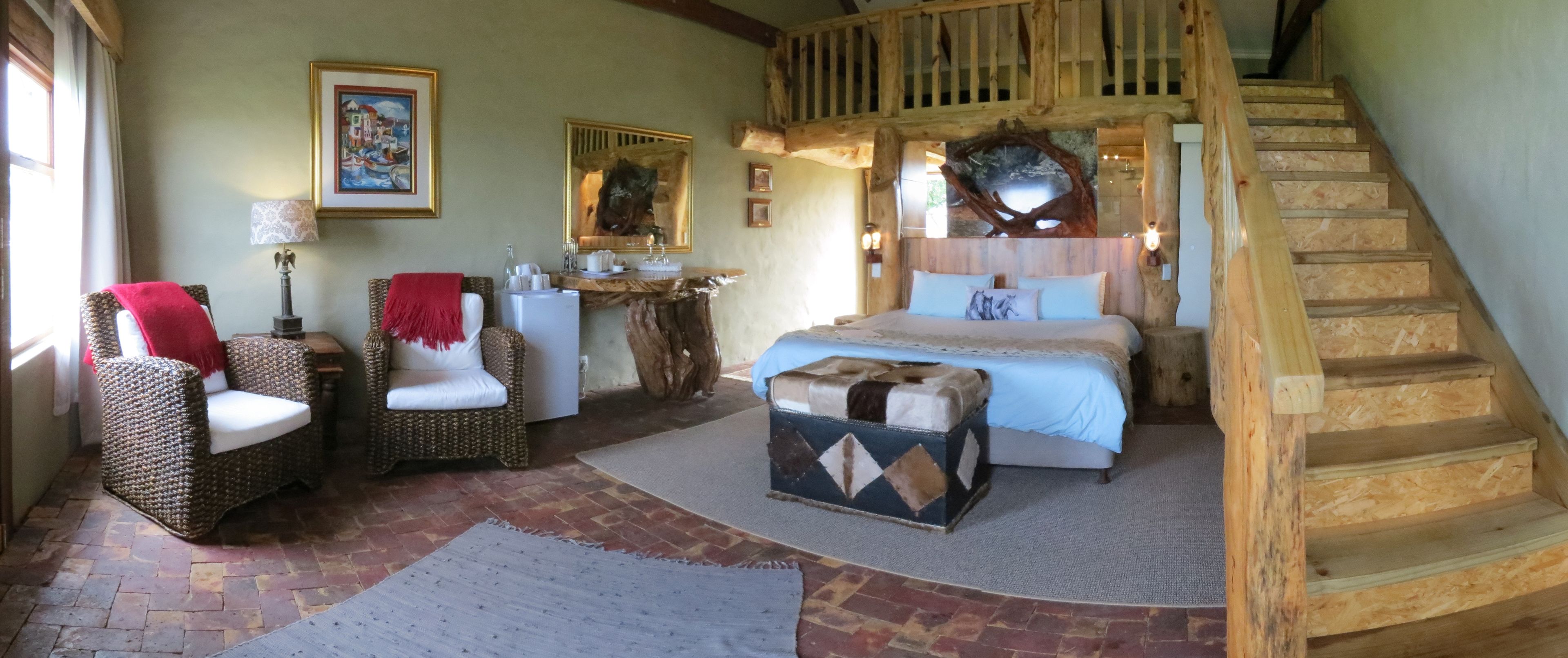 A cozy bedroom with a wooden staircase, wicker furniture, a bed with a blue bedspread, and a rustic decor.