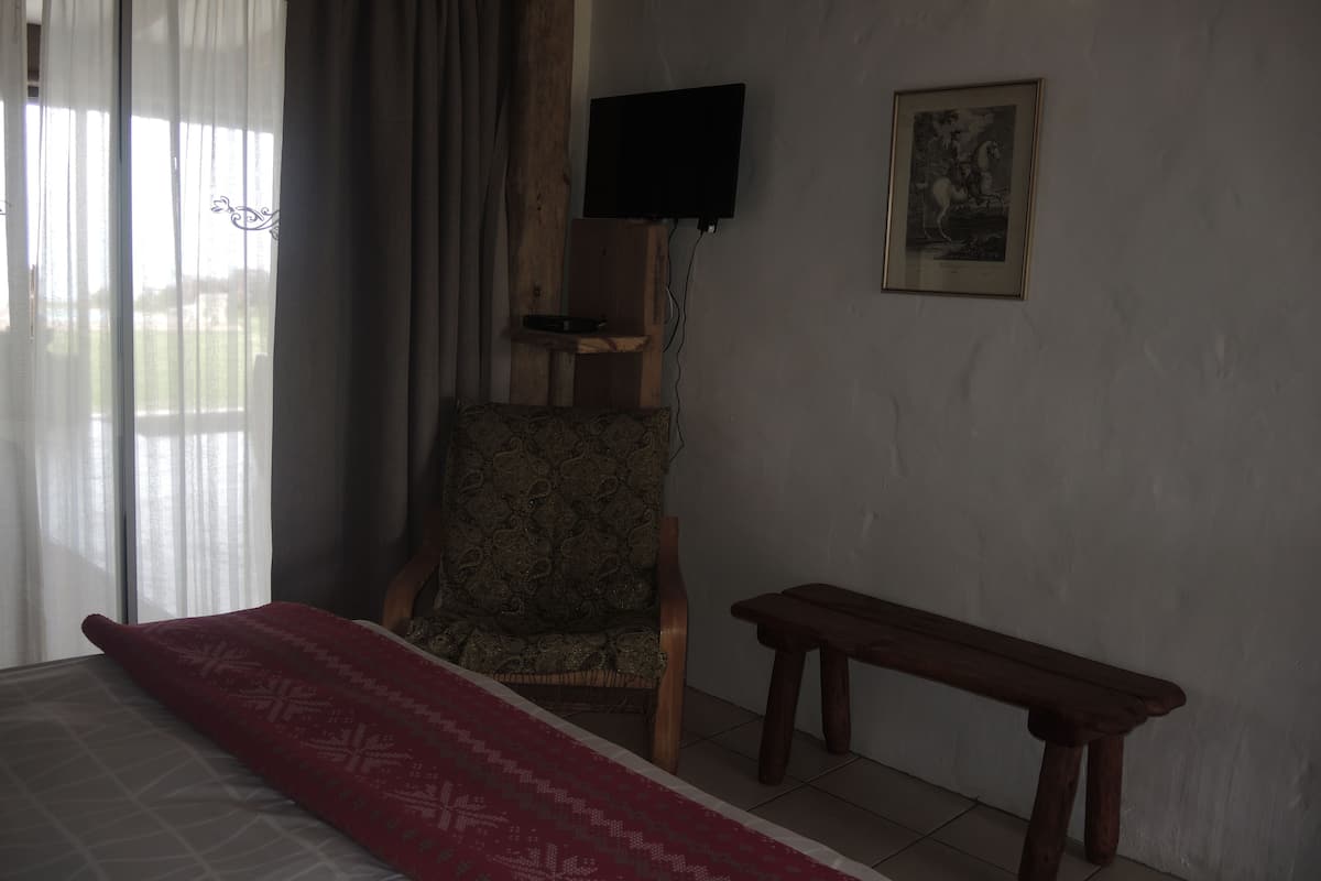 A bedroom with a bed, a chair, a bench, a TV, and a framed picture on the wall.