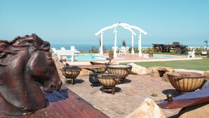 A patio area with outdoor seating, a pool, and a view of the ocean. - T'Niqua Stable Inn (Plettenberg Bay)