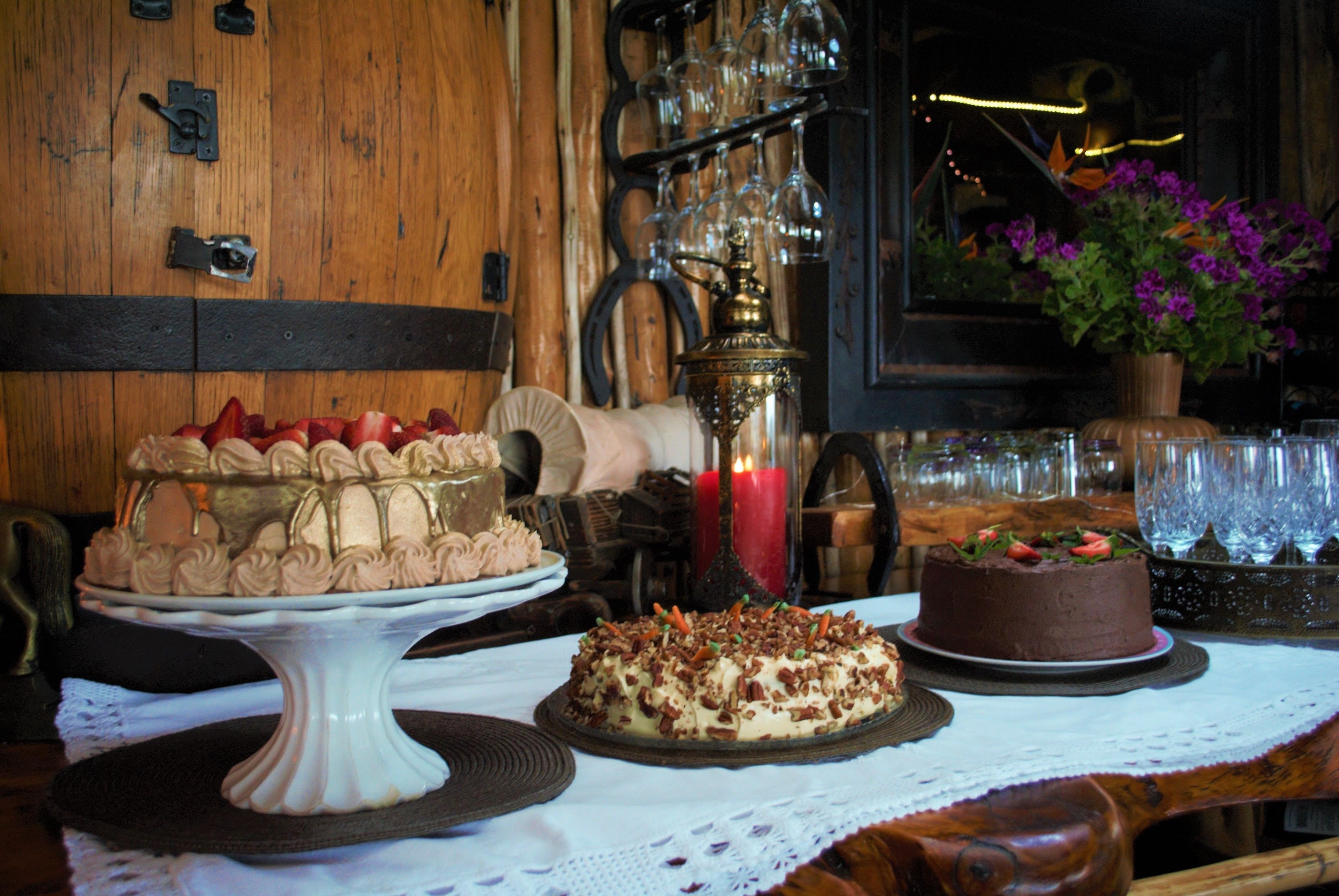 A table with three cakes, a candle, and a vase of flowers.