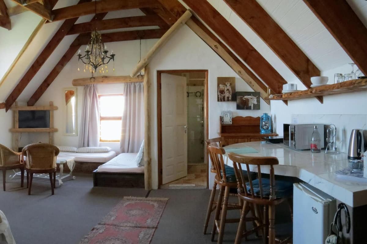 A cozy bedroom with a large bed, a desk, and a chair, a small kitchenette, and a bathroom visible through an open door.