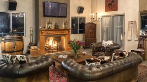 A cozy living room with a fireplace, leather sofas, a television, and a chandelier. - T'Niqua Stable Inn (Plettenberg Bay)