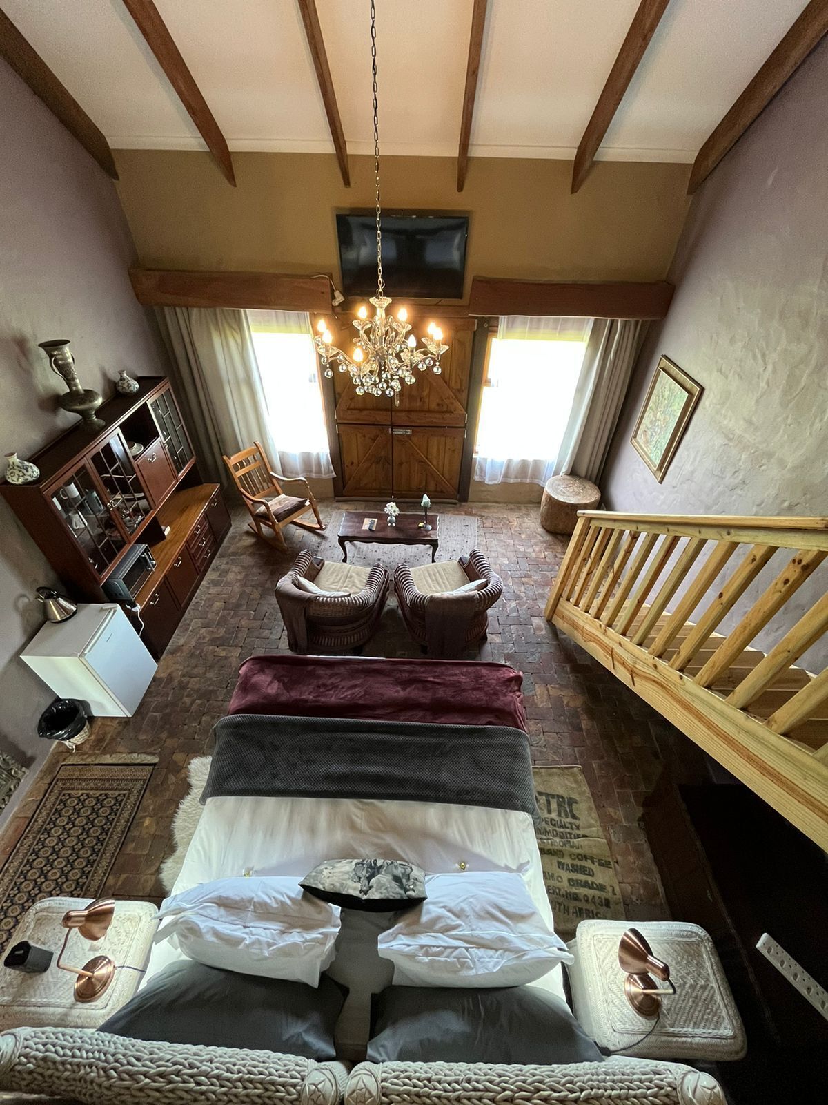 Ein gemütliches Schlafzimmer mit einem Bett, einem Holzstuhl, einem kleinen Tisch, einer Kristallleuchtre und einem an der Wand befestigten Fernseher.