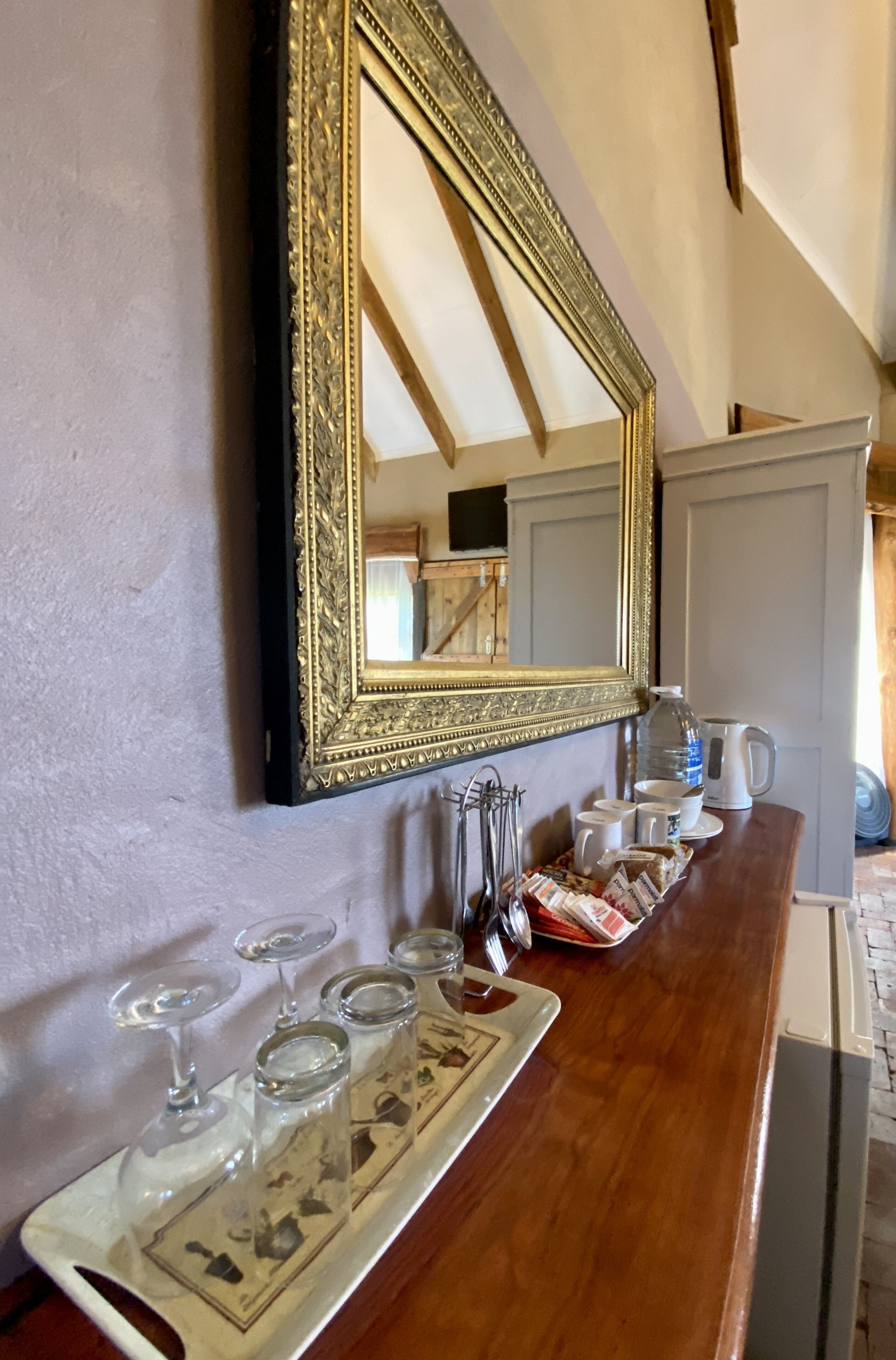 A bar area with a wooden counter, a large ornate mirror, and a tray with wine glasses and a water jug.