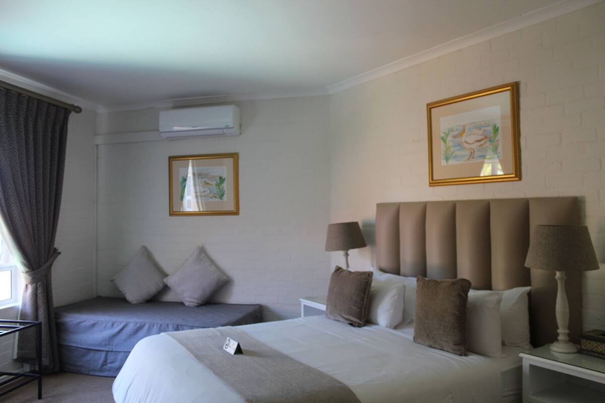 A hotel room with a large bed, a smaller bed, two lamps, and two framed pictures on the wall.