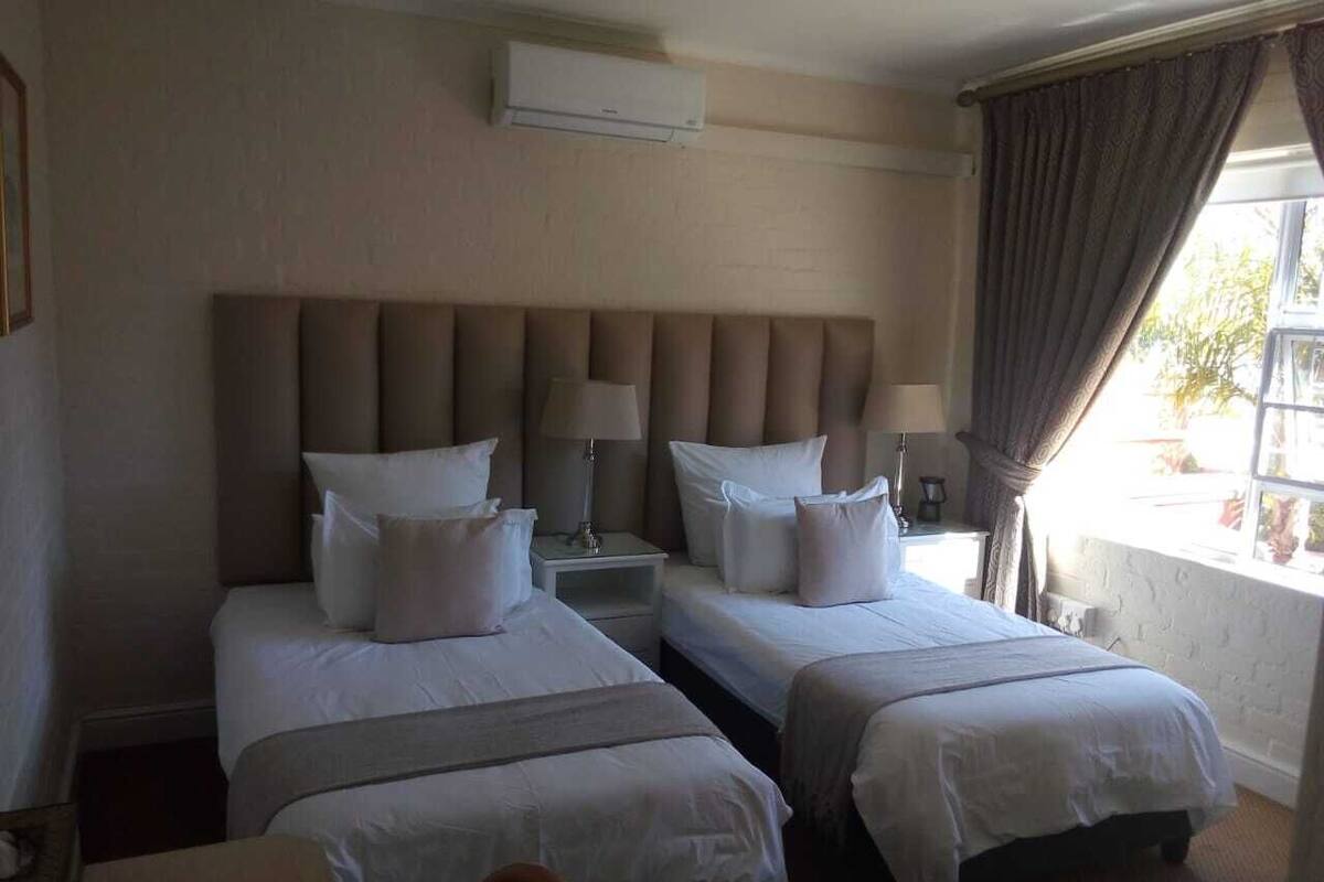 A hotel room with two beds, a nightstand, a lamp, and a window with curtains.
