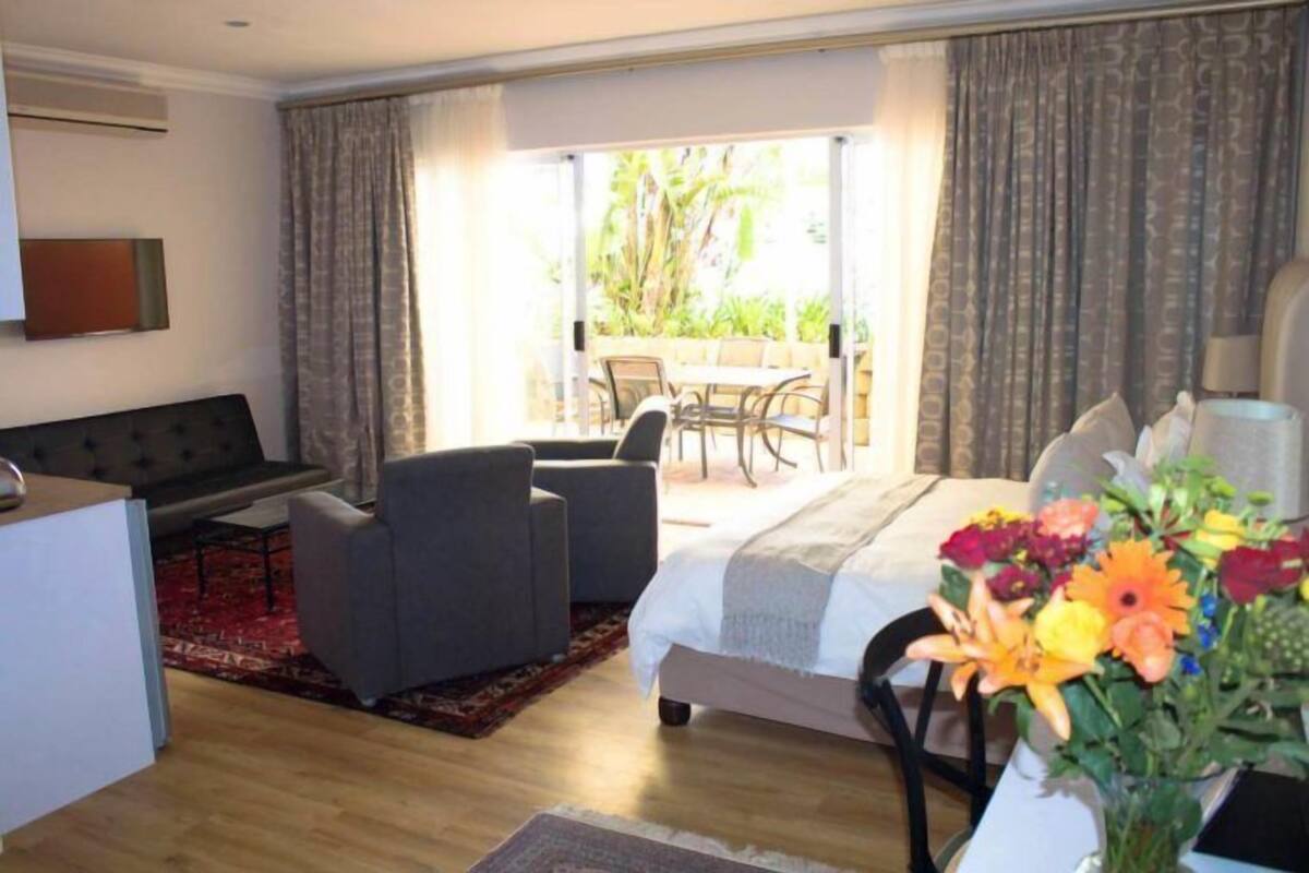 A hotel room with a bed, a desk, a chair, and a dining area with a table and chairs.