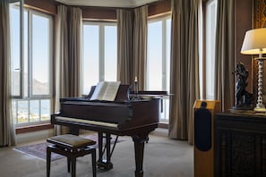 A grand piano with sheet music, a bench, and a statue in a room with large windows and curtains.
