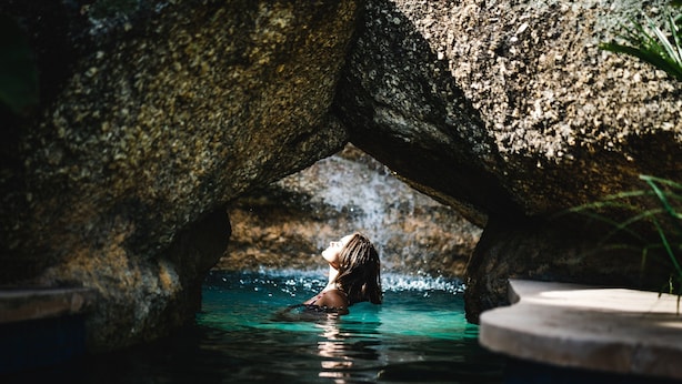 Una persona nada en una piscina natural con una formación rocosa en forma de arco.