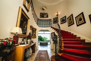 A grand staircase with red carpet leading to an outdoor area, surrounded by framed artwork and a decorative lamp.