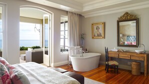 Un dormitorio con una cama grande, una bañera, un tocador con espejo y vista al mar.