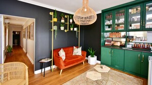 Un salon moderne avec un canapé rouge, un fauteuil en osier, un meuble vert aux portes vitrées et un luminaire suspendu.