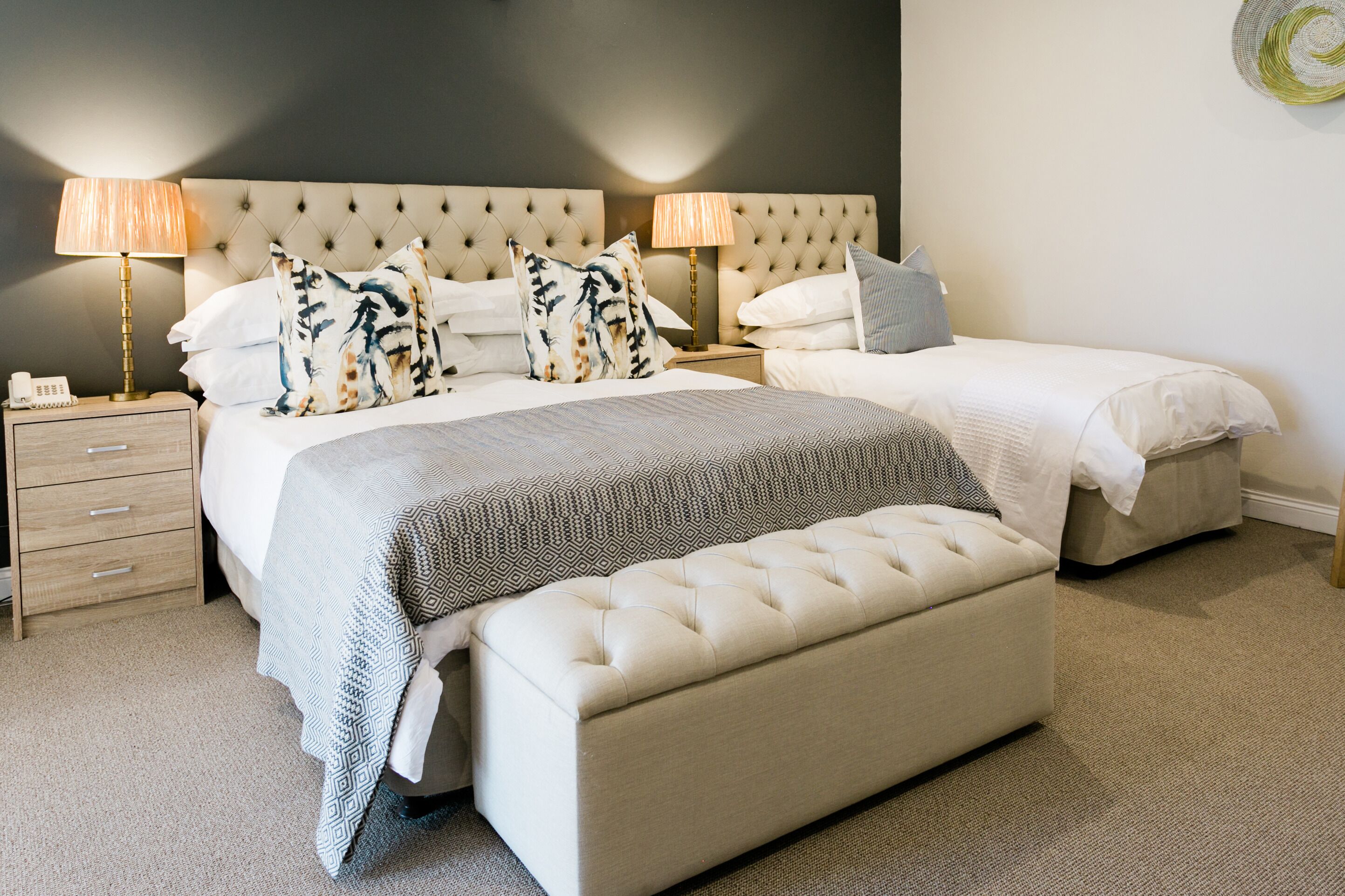 A bedroom with a large bed, two bedside tables, a bench, and a wall-mounted lamp.