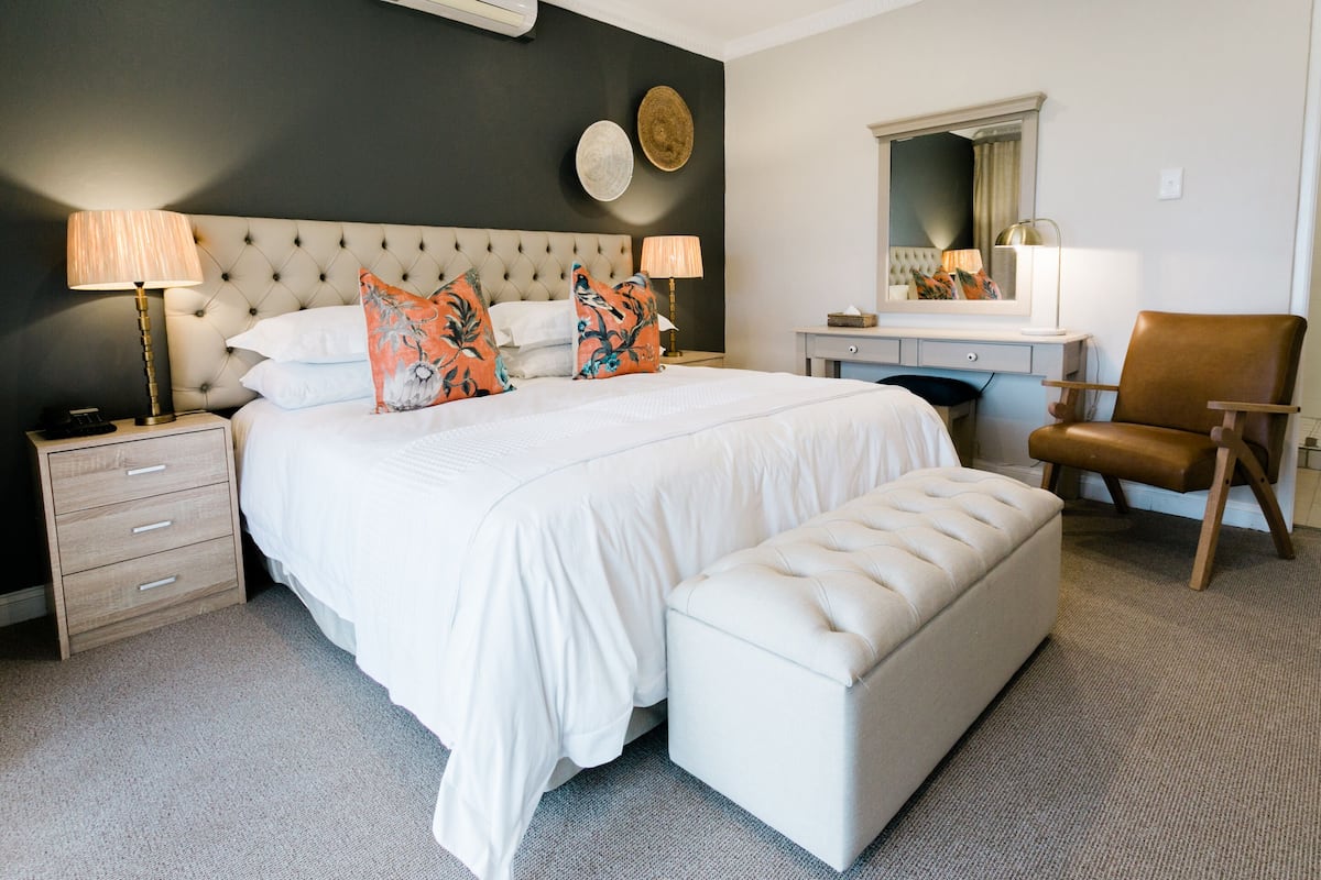 A bedroom with a large bed, bedside lamps, a dresser, a chair, and a mirror.