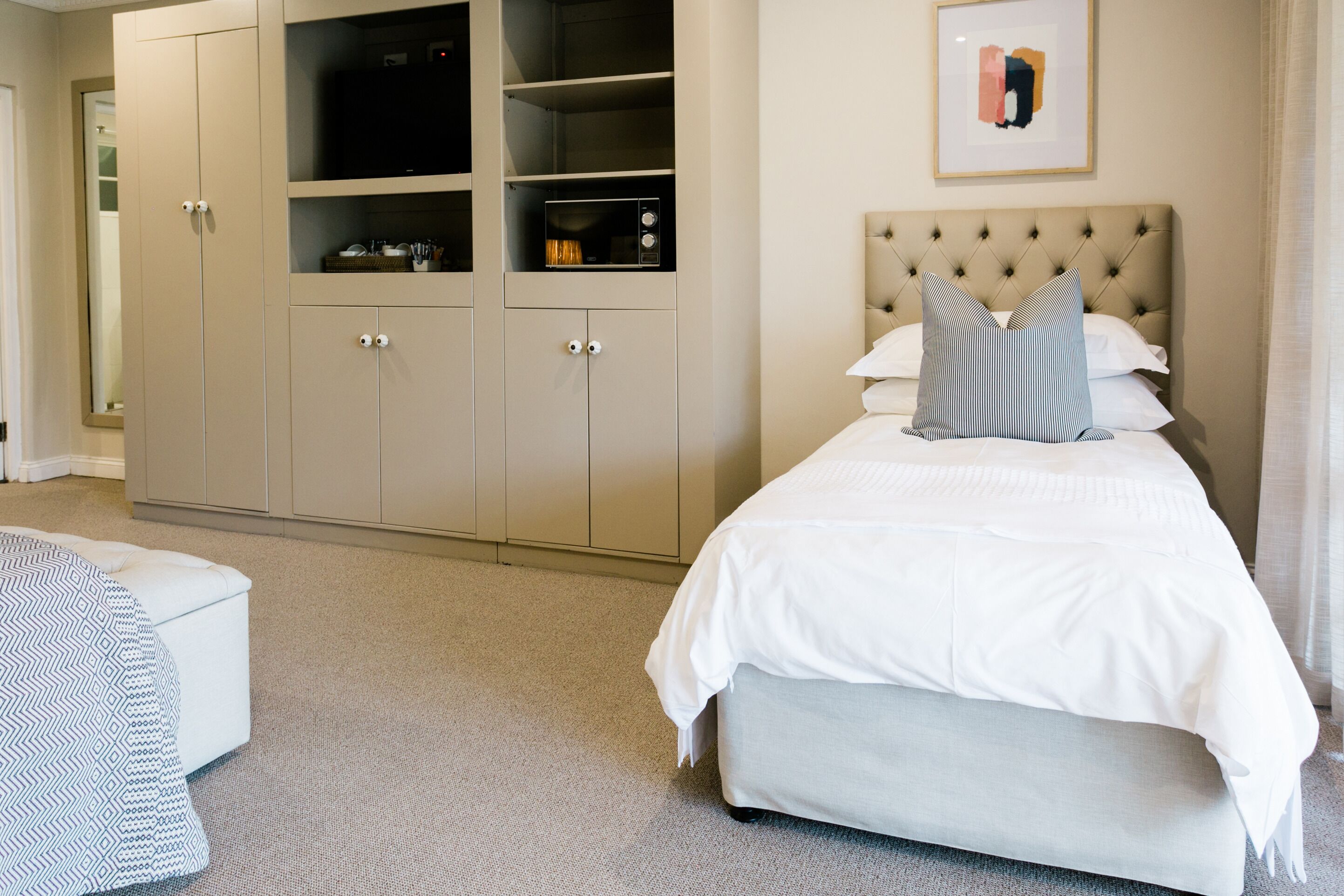 A bedroom with a large bed, a tufted headboard, a chest of drawers, and a framed picture on the wall.