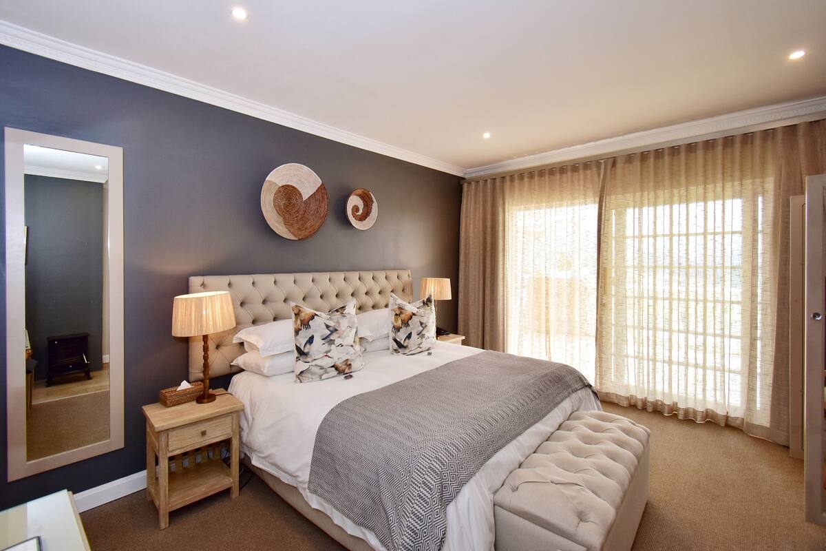 A bedroom with a large bed, two bedside tables, a mirror, and a window with curtains.