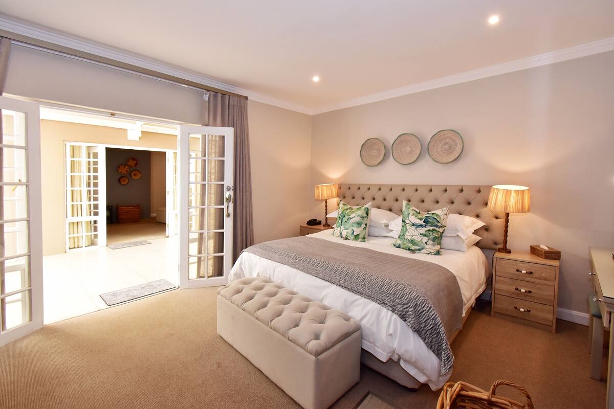 A bedroom with a large bed, a bench, a nightstand, and a door leading to another room.