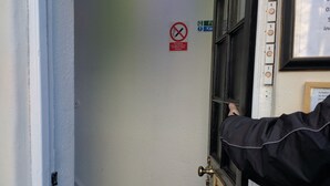 Una porta amb un senyal de prohibició de fumar, un senyal de sortida de foc i un portatarugues amb targeta identificativa.
