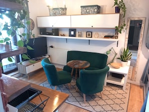 A cozy living room with a green armchair, a small round table, and a white cabinet with decorative items. - Pokoje Gościnne Magnolia (Serock)