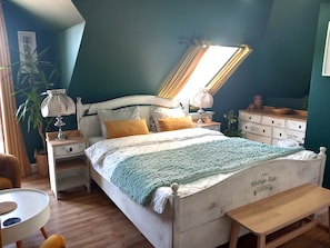 A bedroom with a bed, bedside tables, a lamp, a bench, a dresser, and a window with curtains. - Pokoje Gościnne Magnolia (Serock)