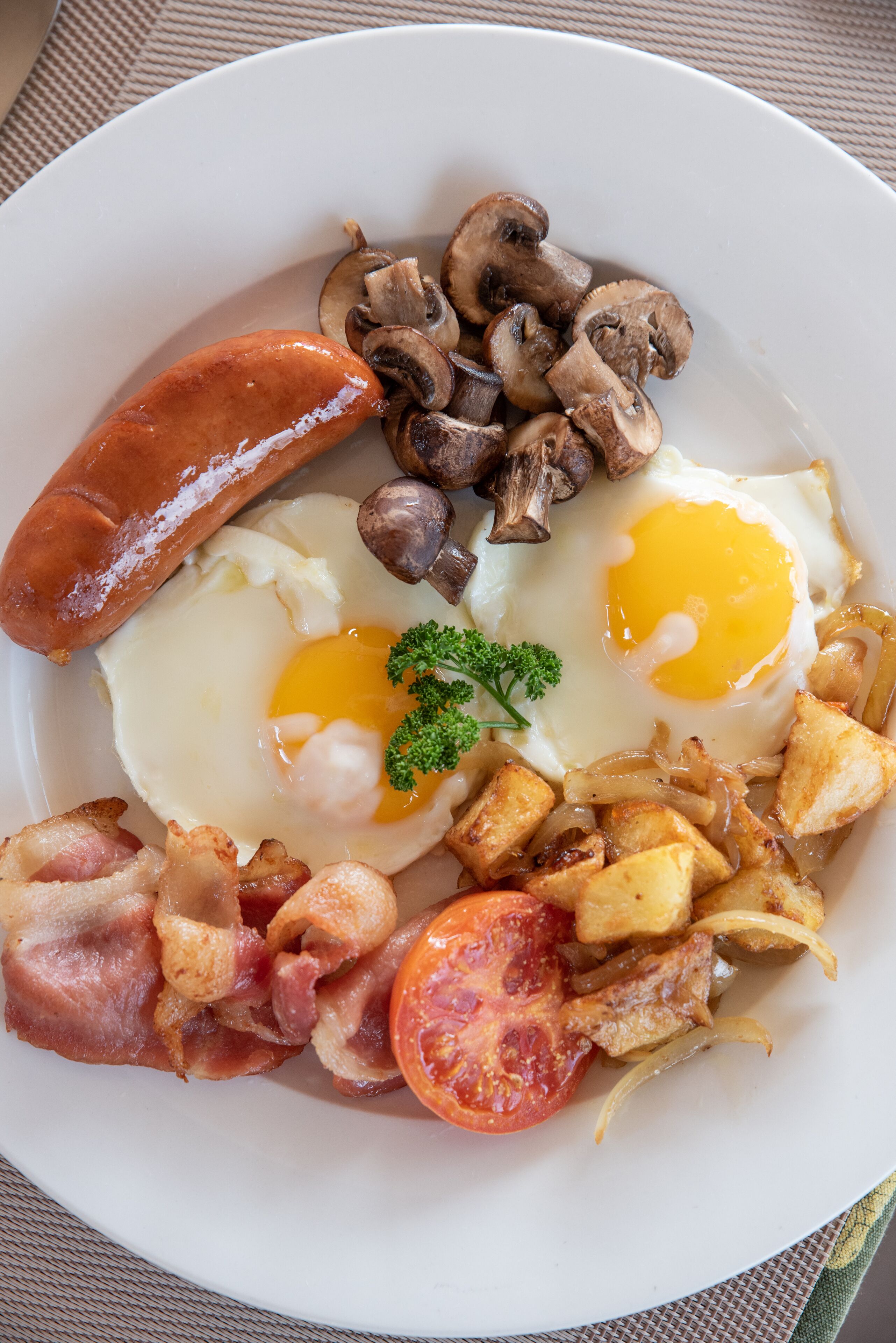 Une assiette de nourriture pour le petit-déjeuner comprenant des œufs, des saucisses, des champignons, du bacon et des tomates.