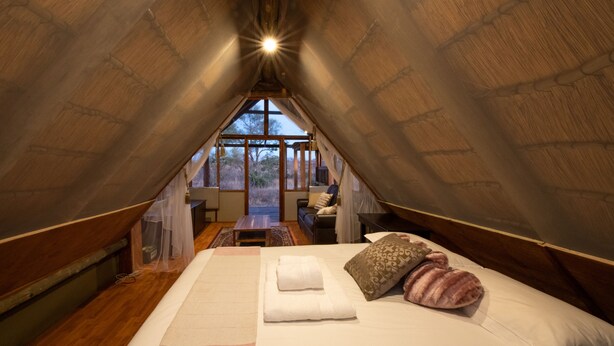 Ein gemütliches Schlafzimmer im Dachgeschoss mit einem großen Bett, Holzboden und Blick ins Freie.