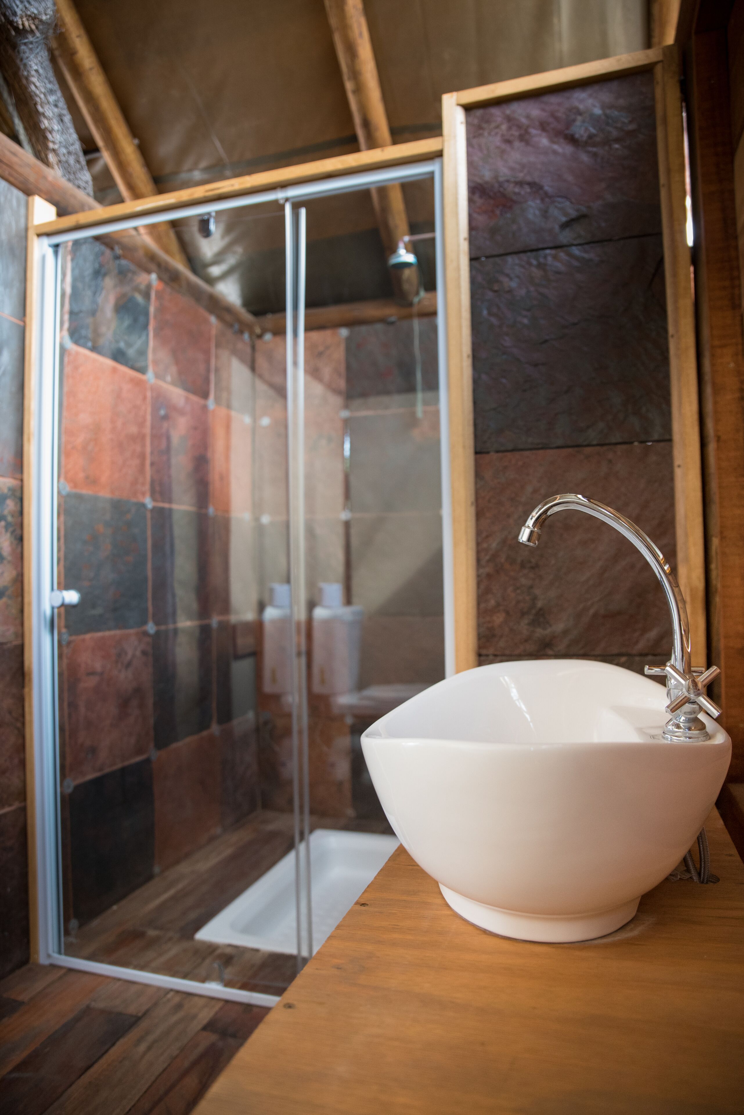 A bathroom with a glass shower enclosure, a white sink, and wooden flooring.