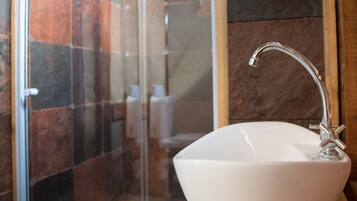 A bathroom with a glass shower enclosure, a white sink, and wooden flooring.