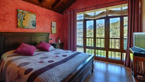 A bedroom with a large bed, wooden headboard, and a view of a mountainous landscape through a large window. - Apartamentos Rurales Balcón Real (Teverga)
