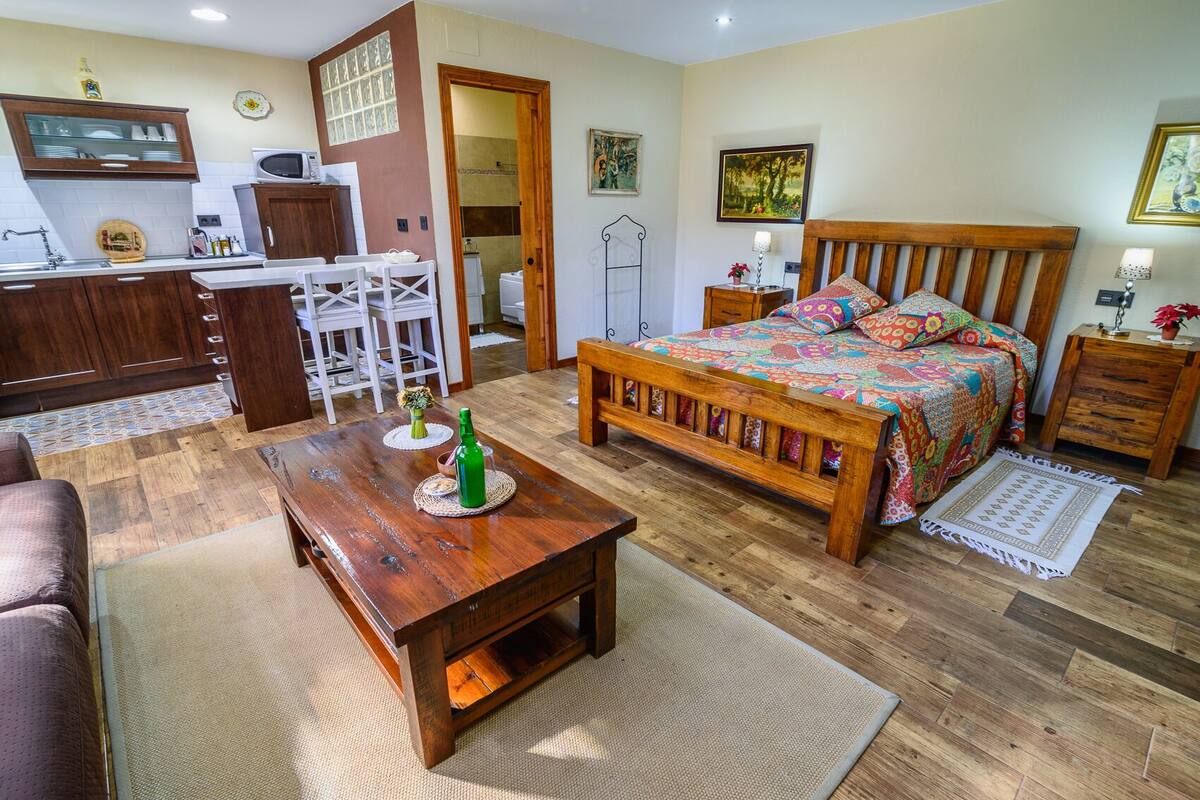 A cozy room with a wooden bed, a dining table, and a kitchen area.
