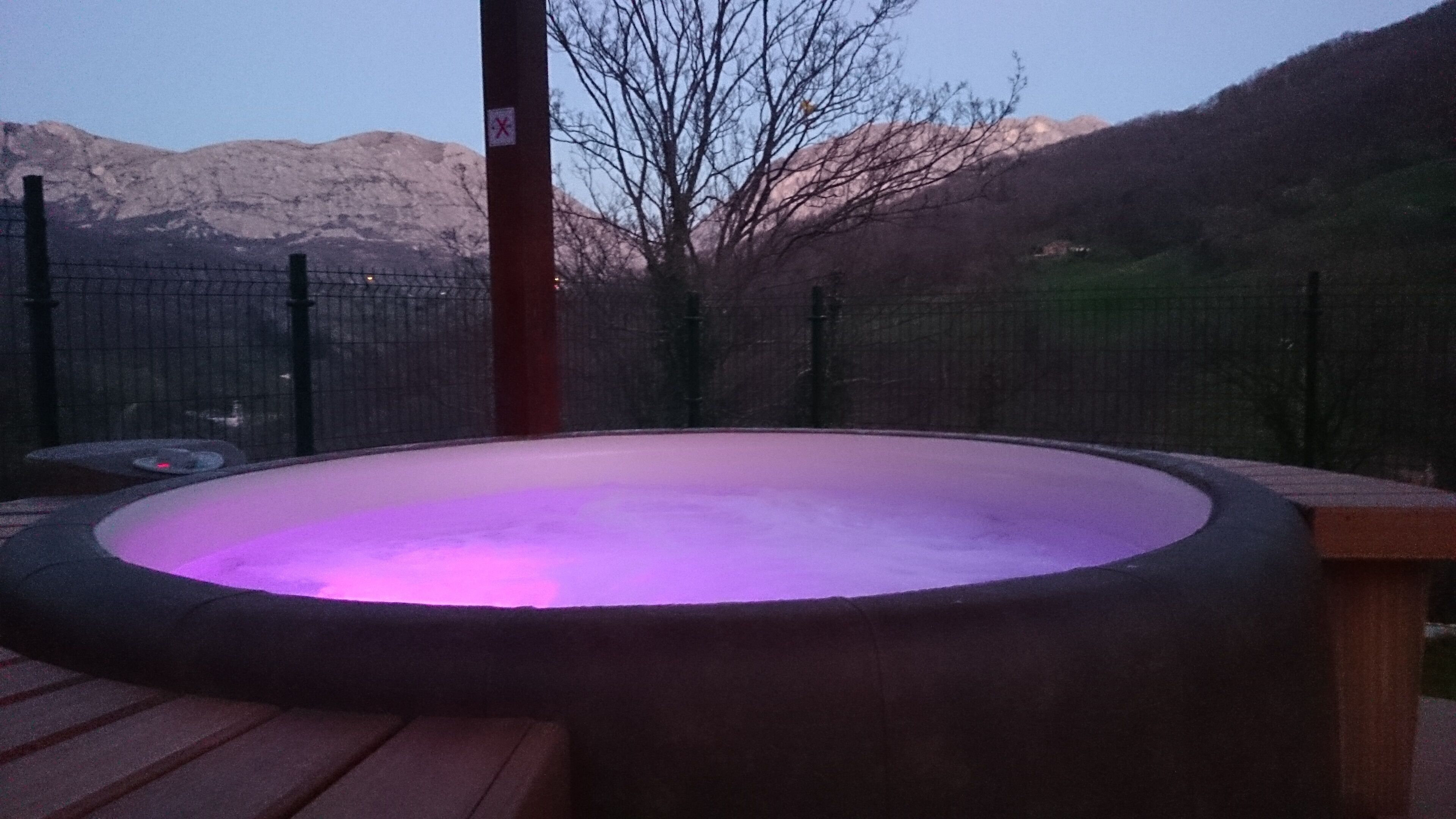A hot tub on a wooden deck with a mountain backdrop.