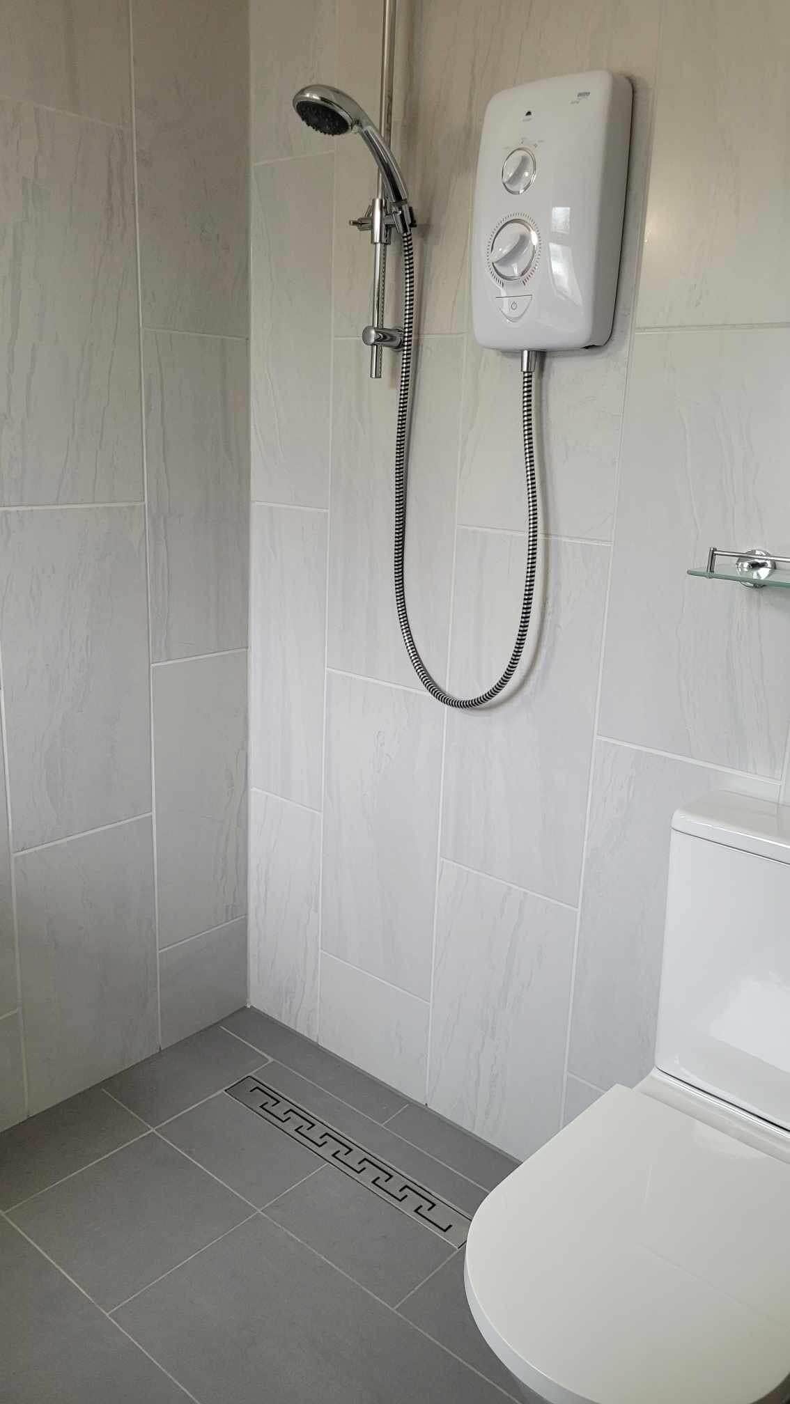 A modern bathroom with a shower, toilet, and a control panel on the wall.