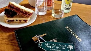 Ein Esstisch mit einem Sandwich, einer Limonadenflasche, einem Glas Wasser und einem ledergebundenen Buch mit dem Etikett 'Gaststätte Kirchenhof'.