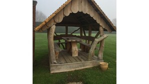 Eine rustikale Holzkonstruktion mit einer Bank und einem Tisch, vermutlich eine Schutzhütte für ein Picknick.