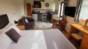 Ein kleines Hotelzimmer mit Bett, Schreibtisch, Stuhl, Kochnische und Fernseher.