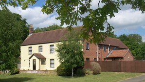 A two-story house with a brick exterior and a tiled roof, surrounded by a well-maintained lawn and a wooden fence. - Church Farm (Norwich)