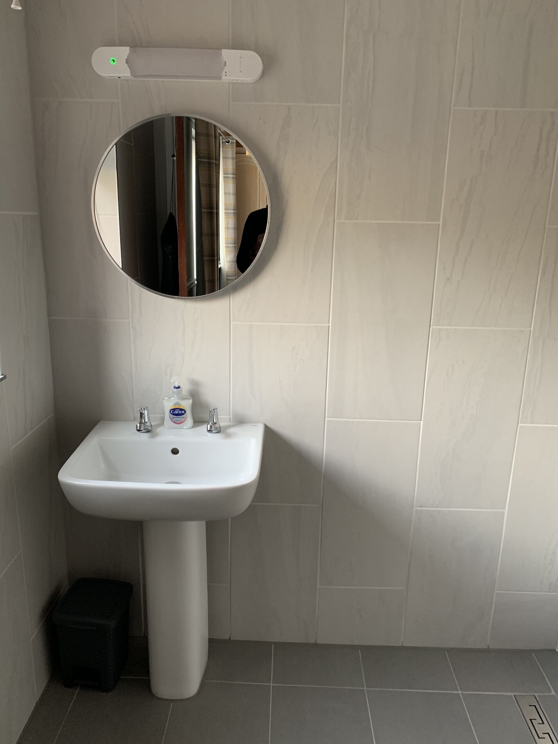 A bathroom with a white pedestal sink, a round mirror, and a light fixture above the mirror.