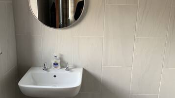 A bathroom with a white pedestal sink, a round mirror, and a light fixture above the mirror.