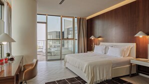 Un hotel moderno con una cama grande, dos lámparas de noche, un escritorio con una silla y vistas de la ciudad a través de amplias ventanas.
