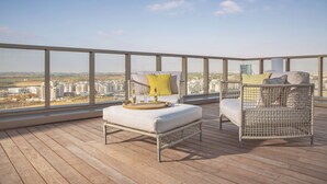 Un balcón con mobiliario de mimbre, piso de madera y vista a la ciudad.