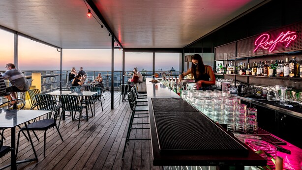 Un bar en la azotea con letrero de neón, terraza de madera y mesas y sillas para los huéspedes.