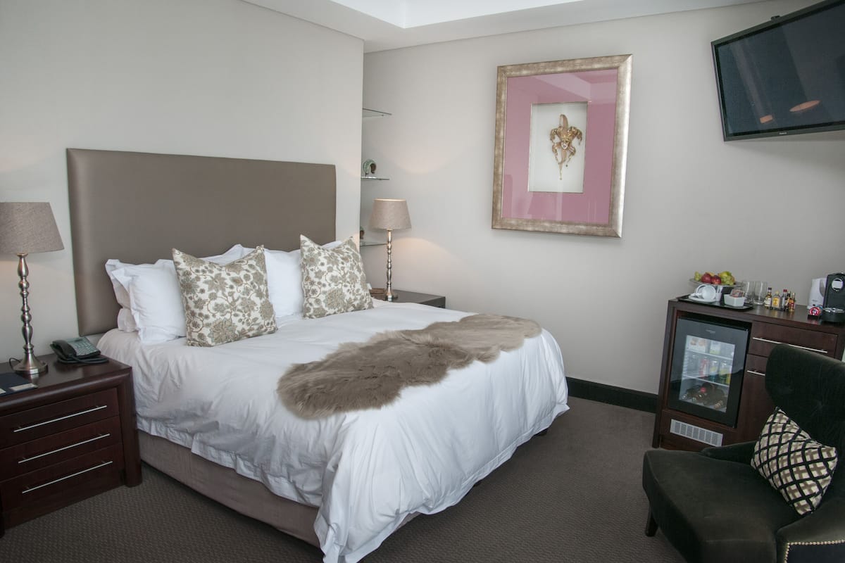 A hotel room with a large bed, bedside lamps, a television, a small refrigerator, and a chair.