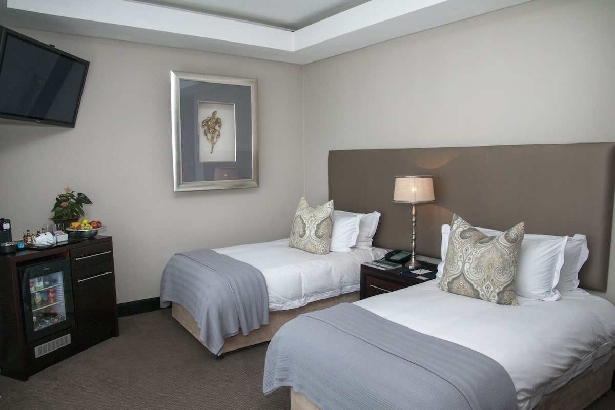 A hotel room with two beds, a television, a small refrigerator, and a framed artwork on the wall.