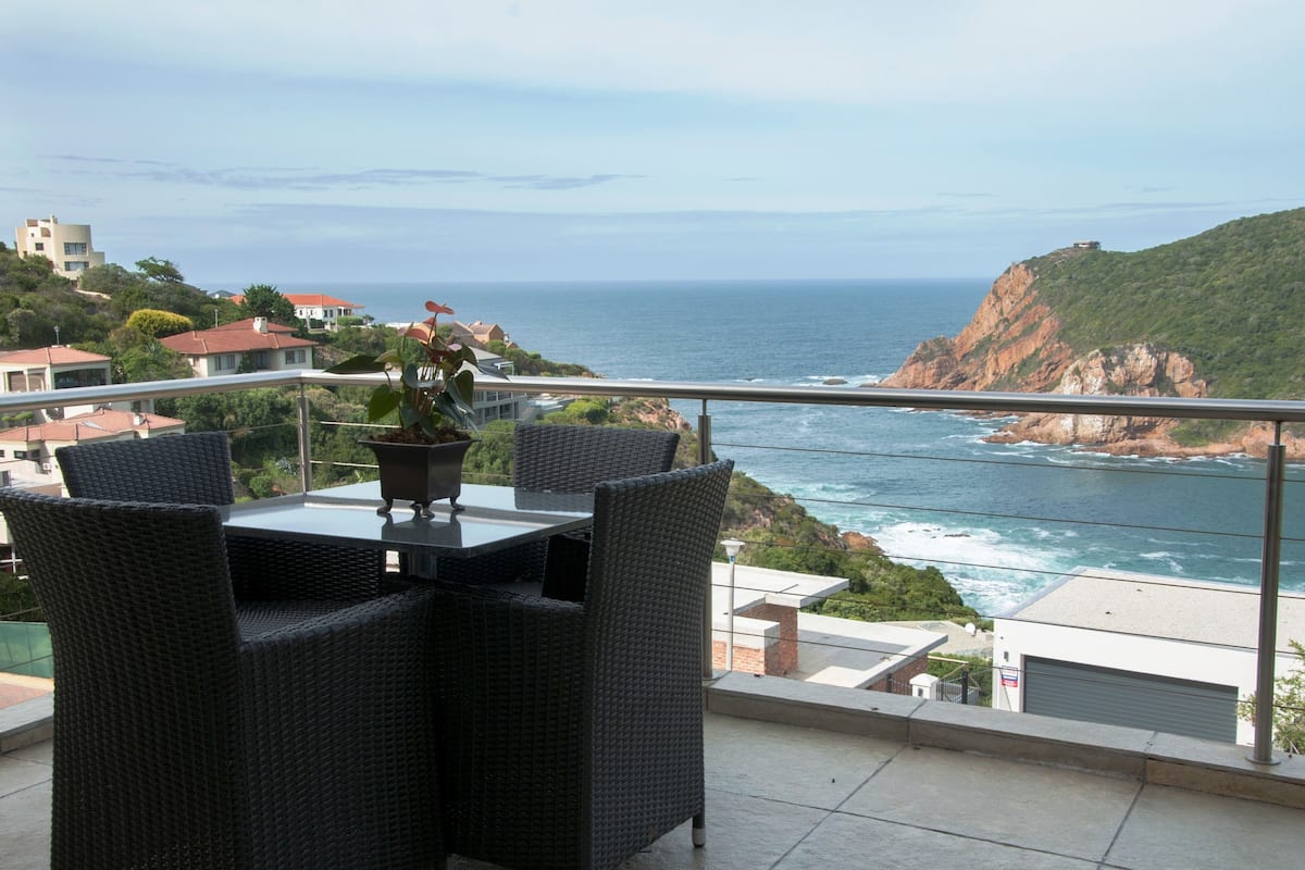 A balcony with wicker furniture overlooking a coastal view.