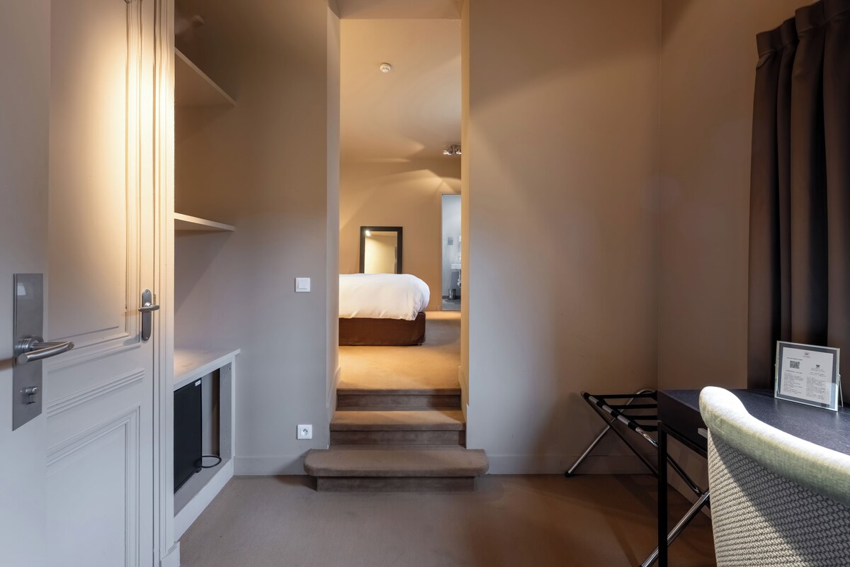 A hotel room with a bed, a desk, a chair, and a small table.
